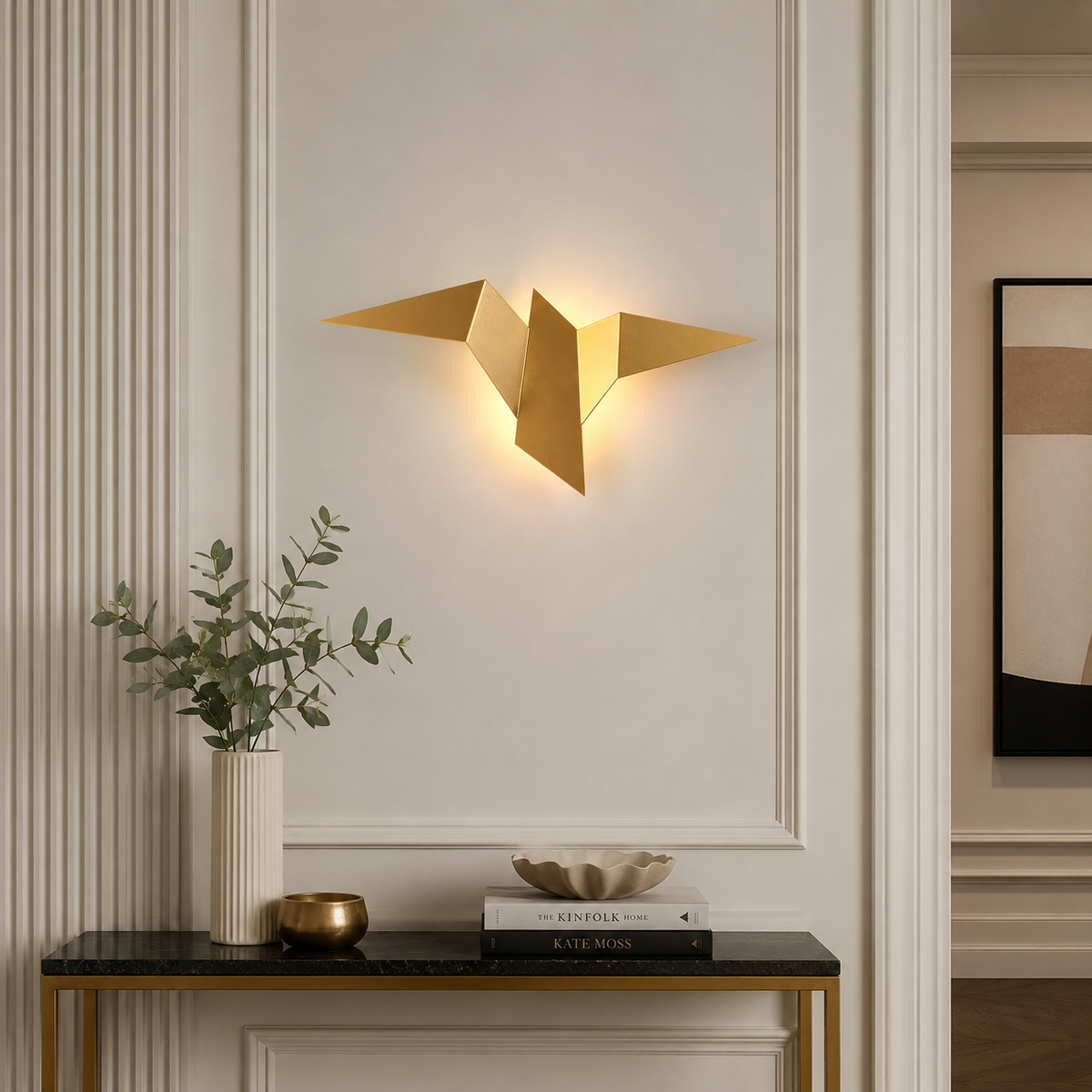 Applique murale originale origami oiseau dorée au-dessus d'une console en marbre noir et laiton, dans une entrée à moulures