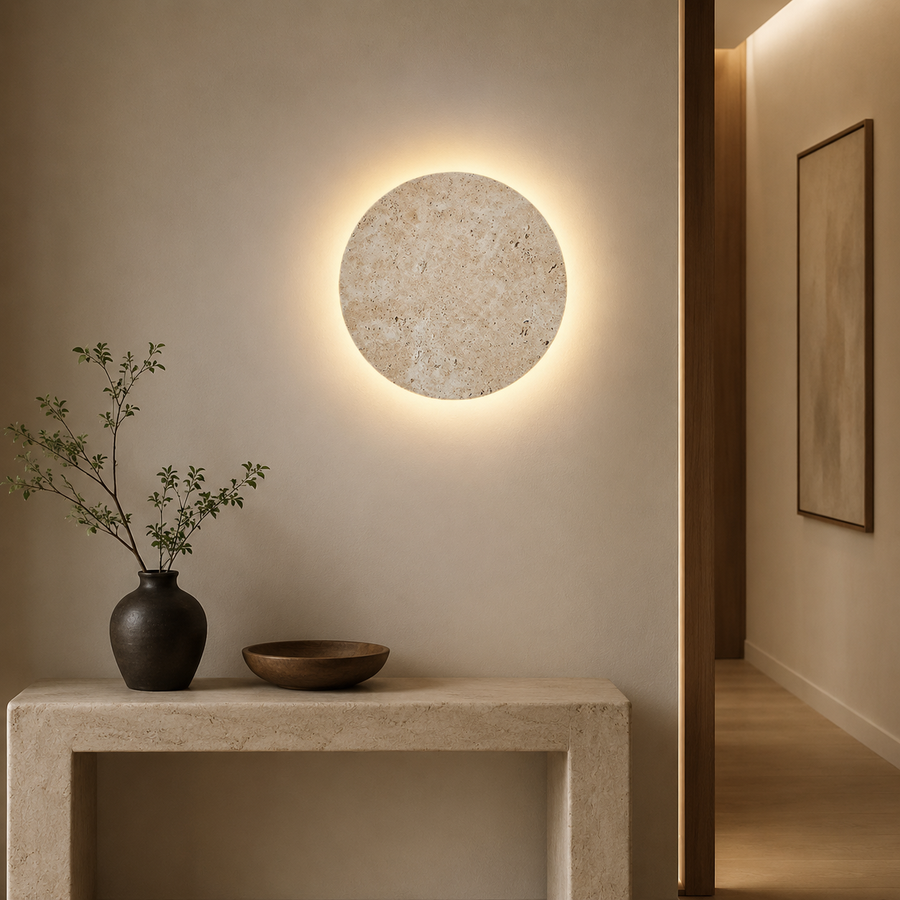 Applique murale ronde en pierre naturelle rétroéclairée au-dessus d'une console d'entrée en travertin, halo chaud sur le mur