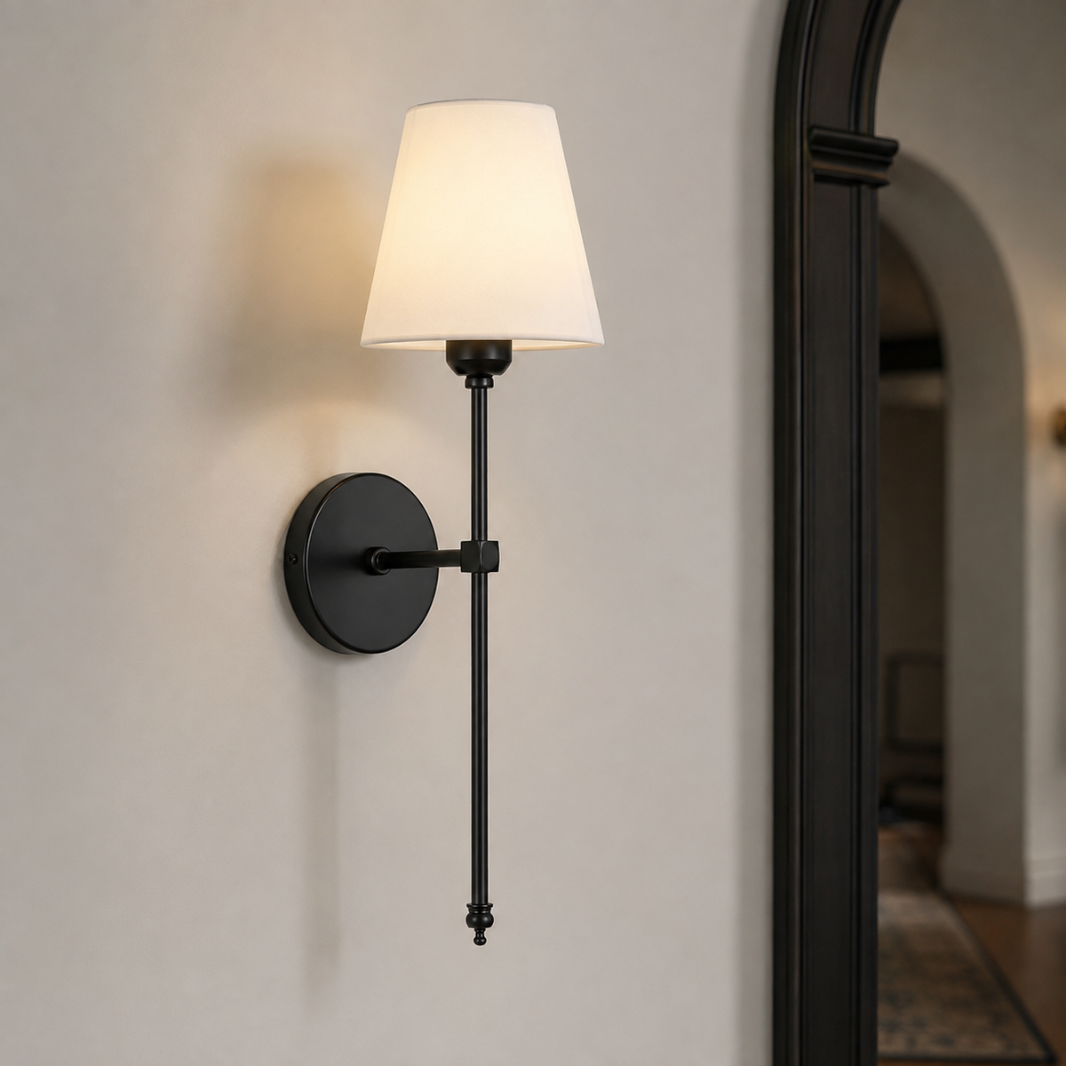 Applique murale vintage noire avec abat-jour en tissu blanc allumée sur un mur clair, près d'une arche